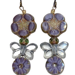 Purple with gold Czech glass Hibiscus flower bead earrings adorned by clear glass butterfly bead with a textured silver edge wash.