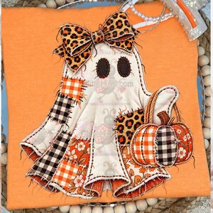 May include: An orange t-shirt featuring a ghost applique with a leopard print bow, dark oval eyes, and a pumpkin basket. The ghost is decorated with patchwork sections of orange and white gingham, black and white buffalo check, and floral patterns.