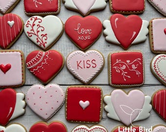May include: Assortment of Valentine's Day sugar cookies decorated with red, pink, and white icing. The cookies are shaped like hearts and squares and feature various designs, including birds, hearts, and the words "love", "kiss", and "xoxo".