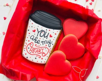 May include: A red gift box filled with cookies decorated with red hearts and a coffee cup cookie that says "You are my heart".