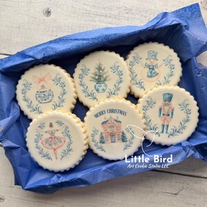 May include: Six round Christmas cookies with white icing and scalloped edges, presented in a blue box. Each cookie is decorated with a different festive design, such as a snowman, a nutcracker, and a house. One cookie has the text "MERRY CHRISTMAS".