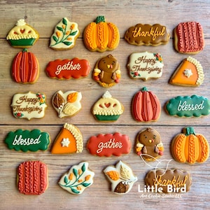 May include: A collection of decorated Thanksgiving cookies. The cookies feature various shapes, including pumpkins, leaves, turkeys, and pie slices. Some cookies have the words "thankful", "gather", and "blessed". The cookies are decorated with orange, green, and brown icing.