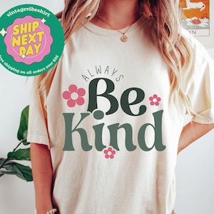 May include: A white t-shirt with the text "ALWAYS Be Kind" in green and pink. The text is surrounded by pink flowers.