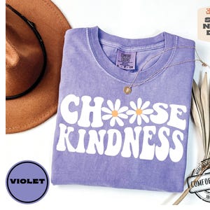 May include: Purple t-shirt with the text "Choose Kindness" in white with a daisy graphic. The shirt is made of 100% cotton.