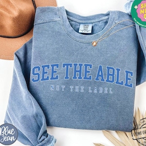May include: A blue sweatshirt with the text "See the Able, Not the Label" in white lettering. The sweatshirt is made of a soft, comfortable fabric and has a vintage look.