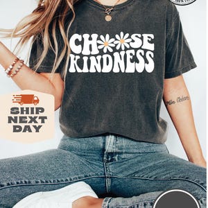 May include: A dark gray t-shirt with the text "Choose Kindness" in white with a daisy graphic. The shirt is made of 100% cotton.