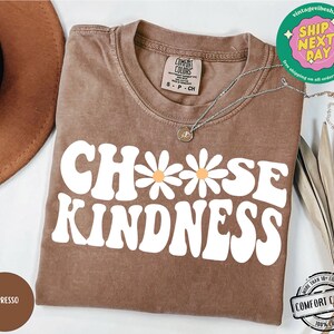 May include: A brown t-shirt with the text "Choose Kindness" in white with a daisy graphic. The shirt is made of 100% cotton.