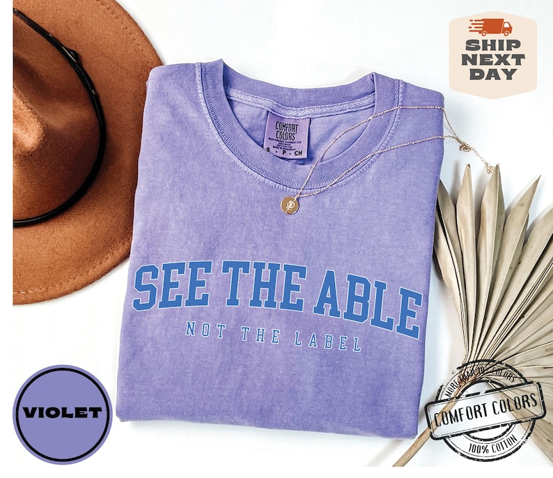 May include: Purple t-shirt with the text "See the Able, Not the Label" in blue lettering. The shirt is made of 100% cotton.