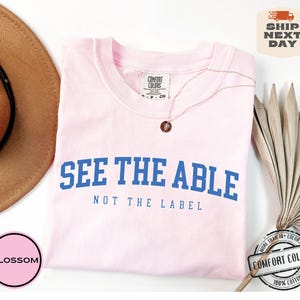 May include: Pink t-shirt with blue text that reads "See the Able Not the Label". The shirt is made of 100% cotton.