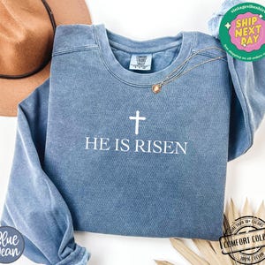 May include: A blue sweatshirt with a white cross and the text "He is Risen".