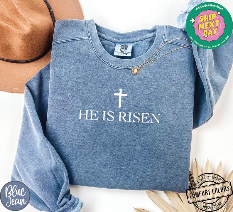 May include: A blue sweatshirt with a white cross and the text "He is Risen".