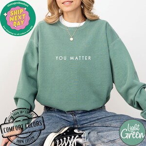 May include: A light green sweatshirt with the text "YOU MATTER" printed in white on the front. The sweatshirt is made of 100% cotton and is available in a variety of colors.
