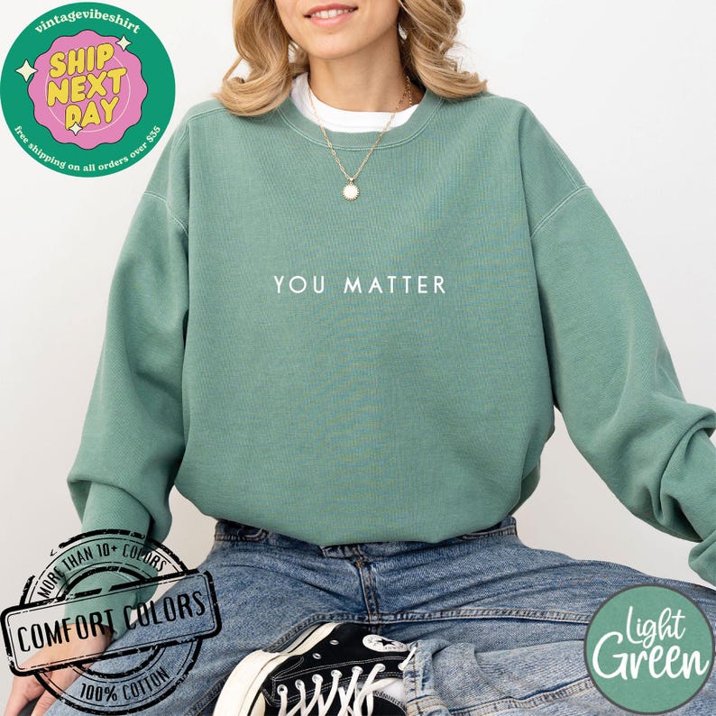 May include: A light green sweatshirt with the text "YOU MATTER" printed in white on the front. The sweatshirt is made of 100% cotton and is available in a variety of colors.