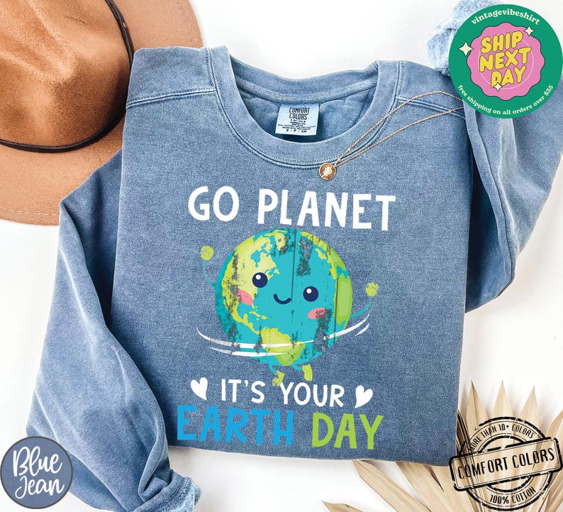 May include: A blue sweatshirt with a cartoon image of the Earth smiling and holding a sign that says "Go Planet It's Your Earth Day".