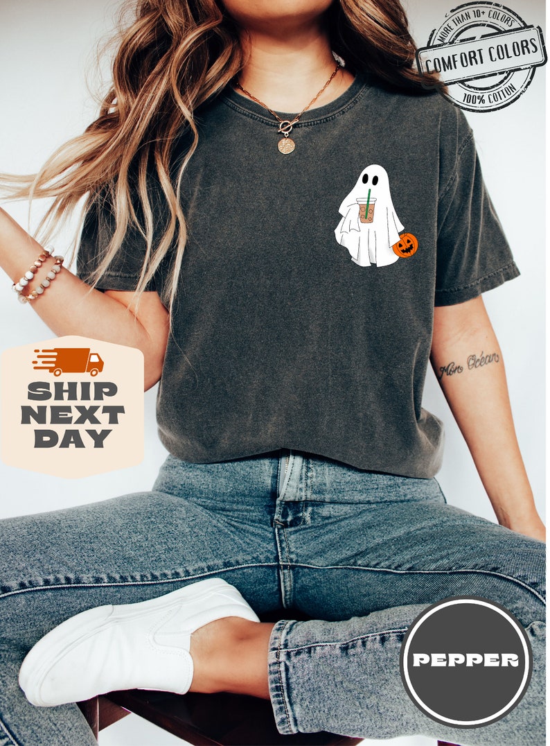 Peut inclure: Un t-shirt gris fonc&eacute; avec un fant&ocirc;me blanc tenant une tasse de caf&eacute; et une petite citrouille. Le t-shirt porte l'inscription "COMFORT COLORS" et "100% COTTON".