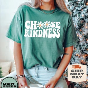 May include: A light green t-shirt with the text "Choose Kindness" in white with a daisy graphic. The text is in a retro font style.