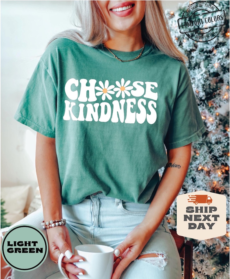 May include: A light green t-shirt with the text "Choose Kindness" in white with a daisy graphic. The text is in a retro font style.
