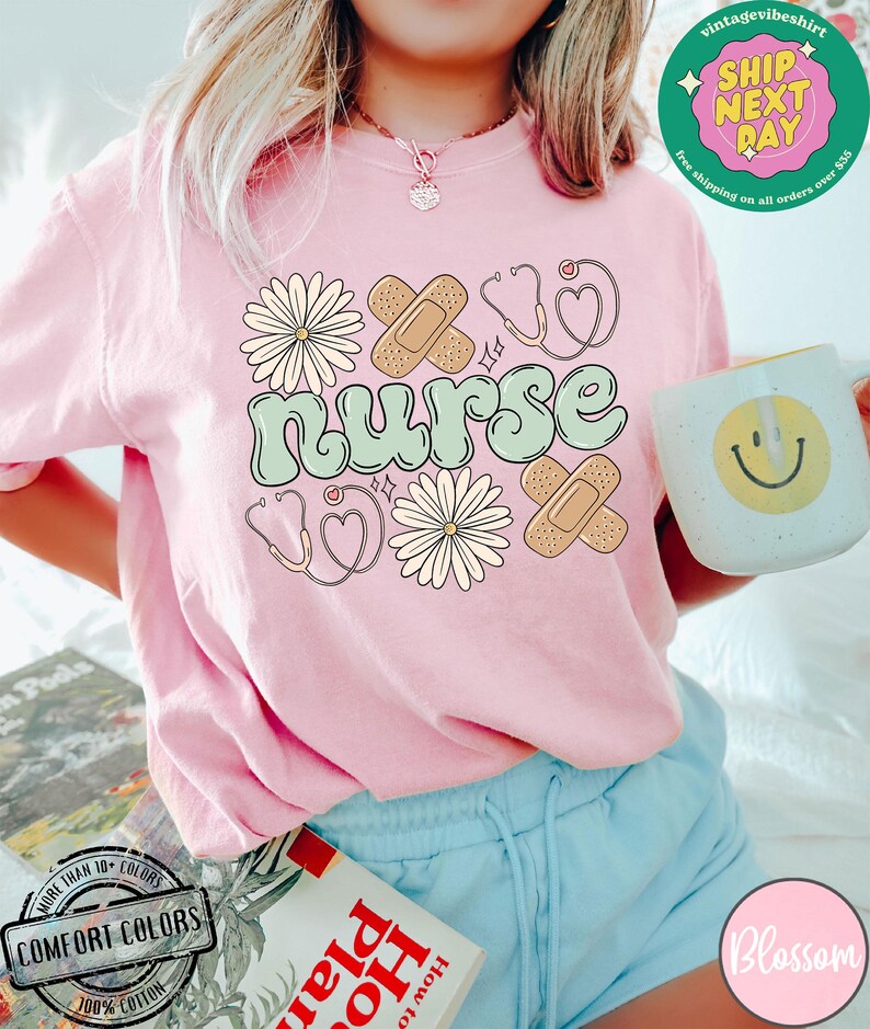 May include: A pink t-shirt with the word "nurse" in green and white lettering. The shirt is decorated with a stethoscope, a heart, bandages, and flowers.