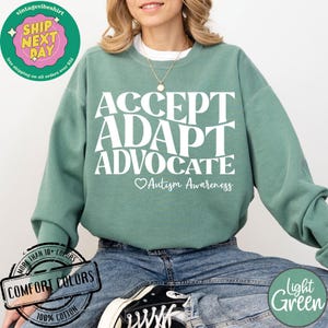 May include: A light green sweatshirt with the words "ACCEPT ADAPT ADVOCATE" in white lettering. Below the words is a heart with the text "Autism Awareness".