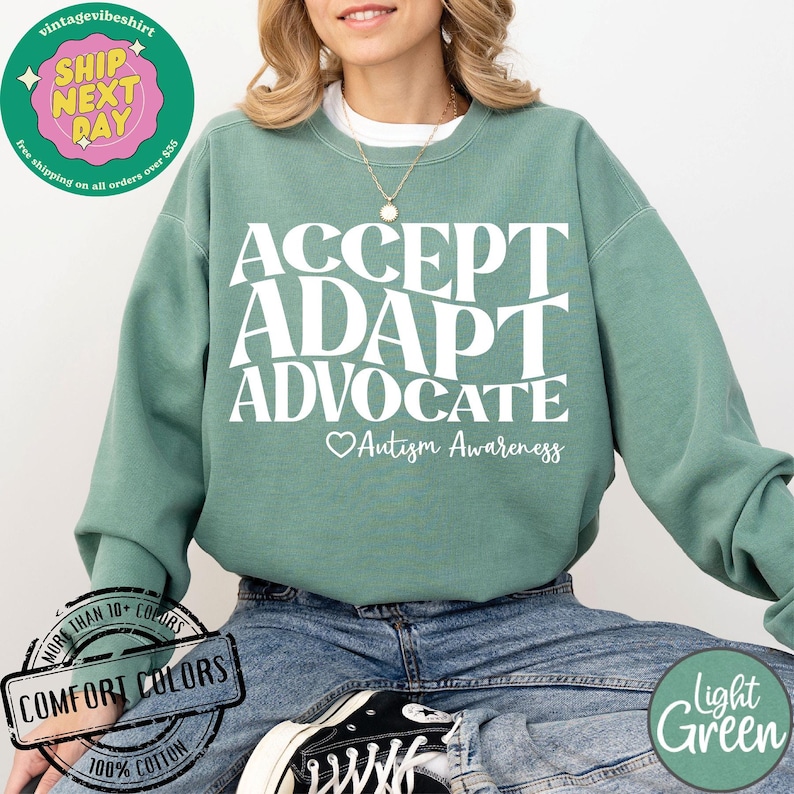 May include: A light green sweatshirt with the words "ACCEPT ADAPT ADVOCATE" in white lettering. Below the words is a heart with the text "Autism Awareness".