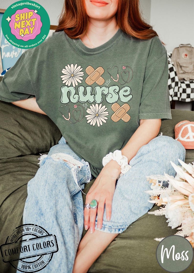 May include: A green t-shirt featuring the word "nurse" in a retro font, surrounded by white daisies, plasters, and stethoscopes. The shirt is made from 100% cotton and is available in a range of colours.