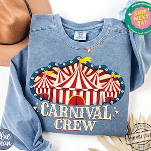 May include: A blue crew neck sweatshirt with a carnival tent graphic in red and white stripes. The text "CARNIVAL CREW" is printed below the graphic in a vintage style font. The sweatshirt has a relaxed fit.