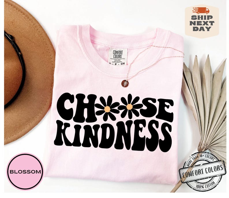 May include: Pink t-shirt with the text "Choose Kindness" in a retro font with three yellow flowers. The shirt is made of 100% cotton.