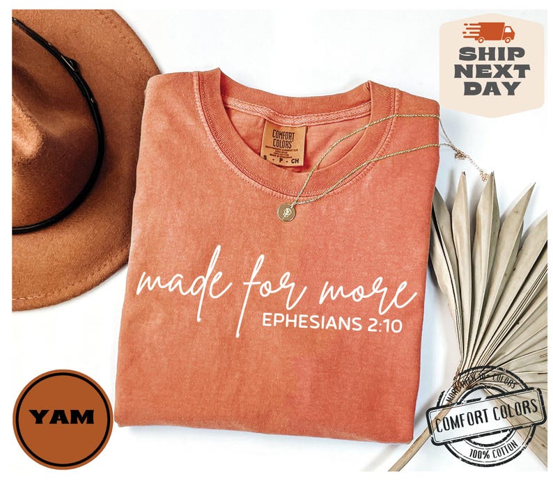 Puede incluir: Una camiseta de color coral con el texto "made for more" y "EPHESIANS 2:10" en blanco. La camiseta est&aacute; hecha de 100% algod&oacute;n.