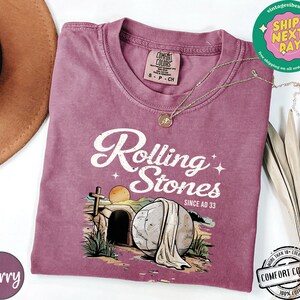 May include: A mauve t-shirt with a vintage-style graphic of a stone rolling away from a tomb. The graphic includes the text "Rolling Stones Since AD 33".