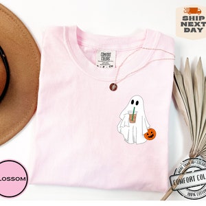 Peut inclure: T-shirt rose avec un fant&ocirc;me blanc tenant une citrouille et une tasse de caf&eacute;. Le t-shirt porte l'inscription "COMFORT COLORS" sur l'&eacute;tiquette.