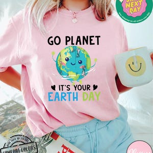 May include: Pink t-shirt with a cartoon image of the Earth holding up a heart with the text "Go Planet It's Your Earth Day".