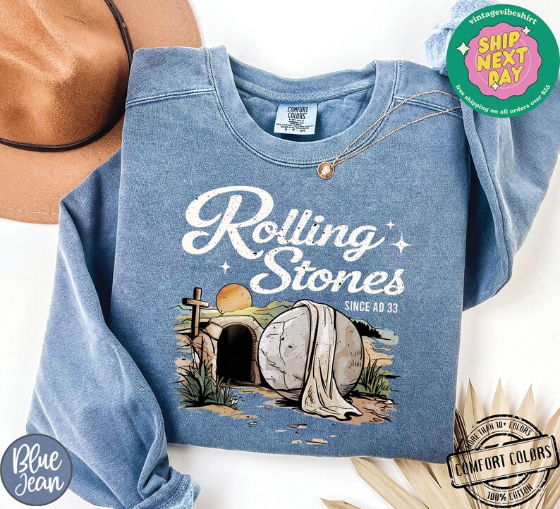May include: A blue sweatshirt with a graphic of a stone tomb with a white cloth draped over it. The text "Rolling Stones Since AD 33" is printed above the image.