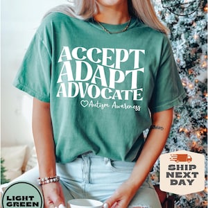 May include: A light green t-shirt with the words "ACCEPT ADAPT ADVOCATE" in white text. Below the words is a heart symbol and the text "Autism Awareness".