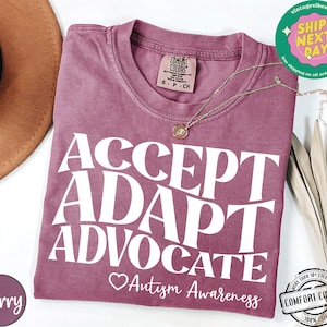 May include: A mauve colored t-shirt with the text "ACCEPT ADAPT ADVOCATE Autism Awareness" in white. The shirt is made of a soft, comfortable material.