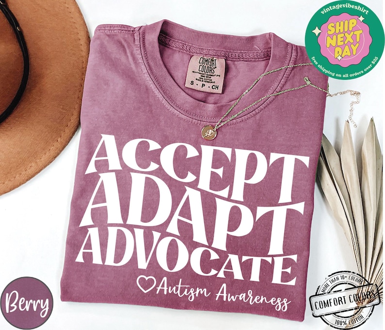 May include: A mauve colored t-shirt with the text "ACCEPT ADAPT ADVOCATE Autism Awareness" in white. The shirt is made of a soft, comfortable material.
