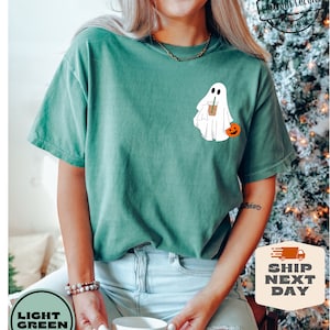 Peut inclure: Un t-shirt vert clair avec un fant&ocirc;me blanc tenant une citrouille et une tasse de caf&eacute;. Le fant&ocirc;me porte un chapeau de paille. Le t-shirt porte le texte "COMFORT COLORS" dans le coin sup&eacute;rieur droit.