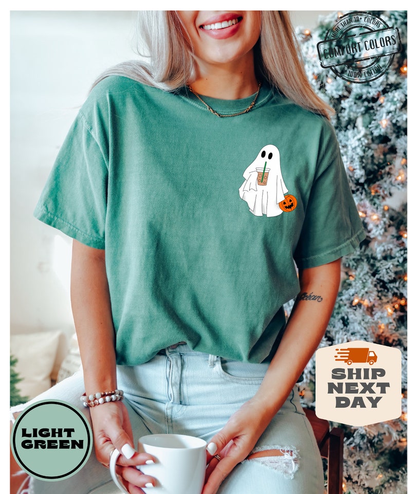 Peut inclure: Un t-shirt vert clair avec un fant&ocirc;me blanc tenant une citrouille et une tasse de caf&eacute;. Le fant&ocirc;me porte un chapeau de paille. Le t-shirt porte le texte "COMFORT COLORS" dans le coin sup&eacute;rieur droit.