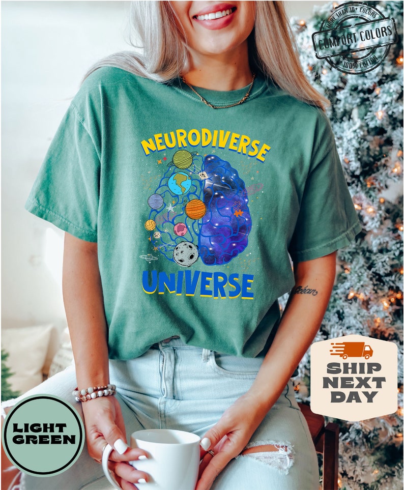 Op de afbeelding: Een lichtgroen T-shirt met een afbeelding van een brein met planeten en sterren erin. De tekst "Neurodiverse Universe" staat op het T-shirt gedrukt.