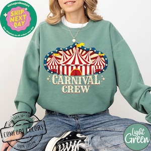 May include: A light green sweatshirt with a carnival tent graphic and the words "CARNIVAL CREW". The graphic features red and white striped tents with a blue border. The sweatshirt is made of 100% cotton.