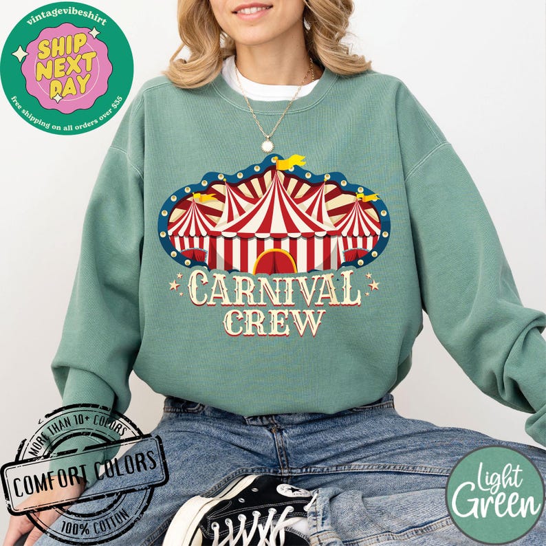 May include: A light green sweatshirt with a carnival tent graphic and the words "CARNIVAL CREW". The graphic features red and white striped tents with a blue border. The sweatshirt is made of 100% cotton.