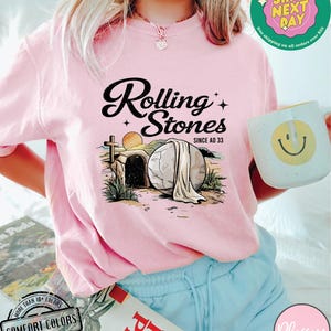 May include: Pink t-shirt with a graphic of a stone tomb with the text "Rolling Stones Since AD 33".