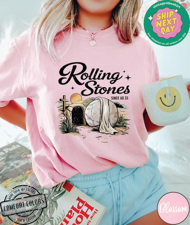 May include: Pink t-shirt with a graphic of a stone tomb with the text "Rolling Stones Since AD 33".