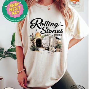 May include: A white t-shirt with a graphic of a stone tomb with a cross and the text "Rolling Stones Since AD 33".