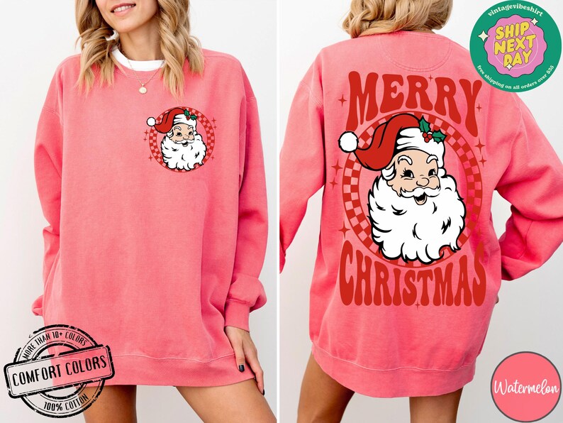 May include: A pink sweatshirt with a vintage-style Christmas graphic on the back. The graphic features a red and white Santa Claus with the text "Merry Christmas". The front of the sweatshirt has a smaller image of Santa Claus.