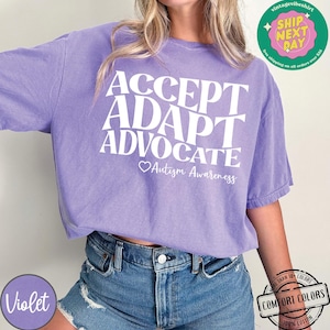 May include: Purple t-shirt with the words "ACCEPT ADAPT ADVOCATE" in white lettering and a heart with the text "Autism Awareness" below.