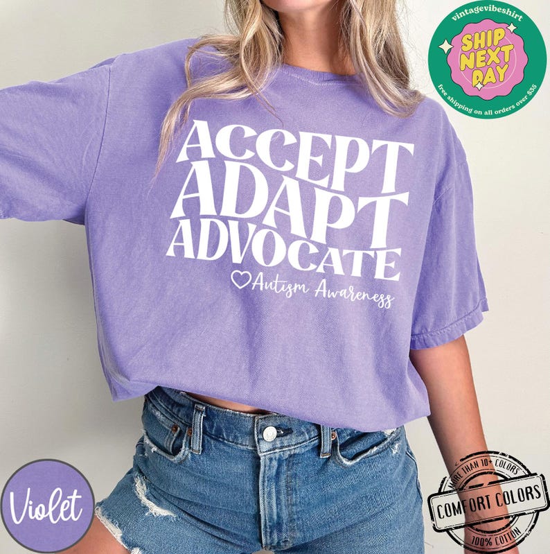 May include: Purple t-shirt with the words "ACCEPT ADAPT ADVOCATE" in white lettering and a heart with the text "Autism Awareness" below.