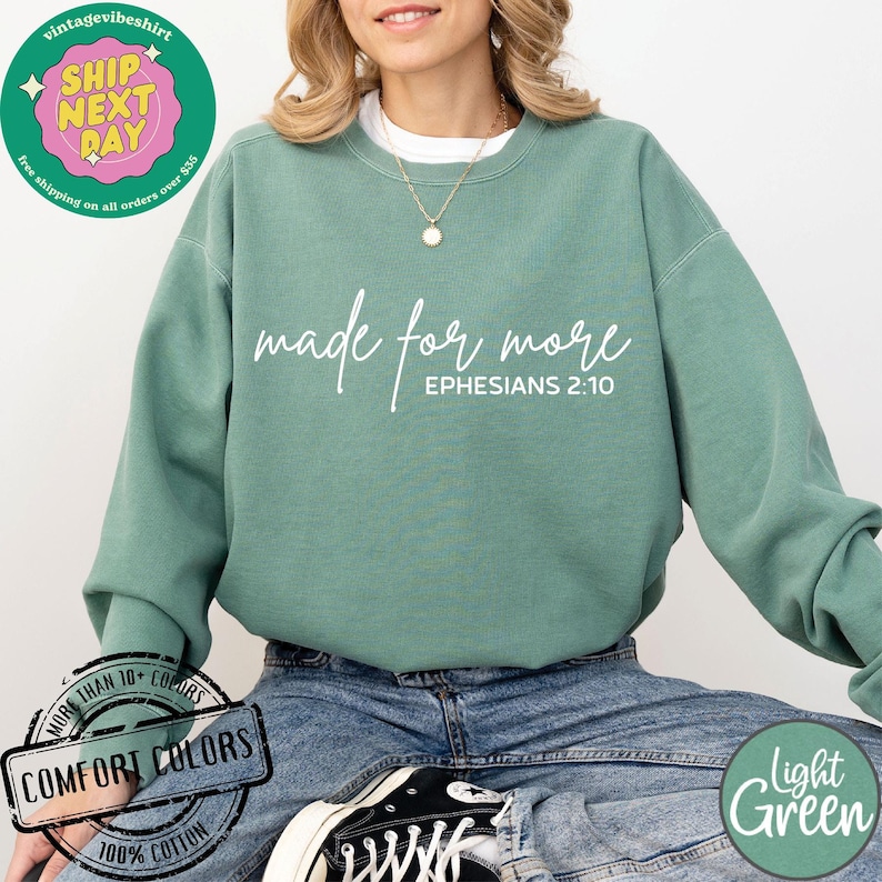 Puede incluir: Una sudadera de color verde claro con el texto "made for more" y "EPHESIANS 2:10" en blanco. La sudadera est&aacute; hecha de 100% algod&oacute;n y est&aacute; disponible en una variedad de colores.