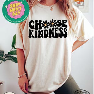 May include: A white t-shirt with the text "Choose Kindness" in black with three yellow daisies. The text is in a retro font style.