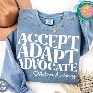May include: A blue sweatshirt with the text "ACCEPT ADAPT ADVOCATE" in white. Below the text is a heart and the words "Autism Awareness".