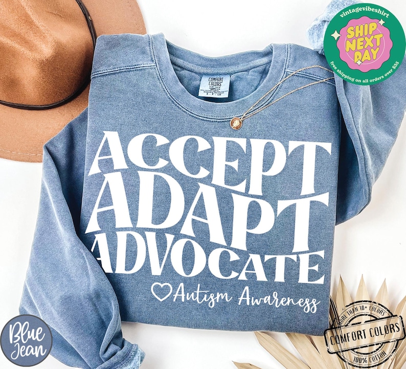 May include: A blue sweatshirt with the text "ACCEPT ADAPT ADVOCATE" in white. Below the text is a heart and the words "Autism Awareness".